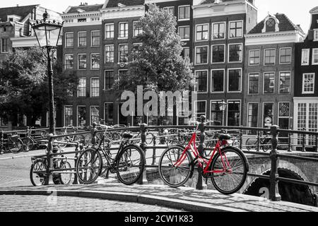 Una foto di una bici rossa sul ponte sul canale di Amsterdam. Lo sfondo è bianco e nero. Foto Stock