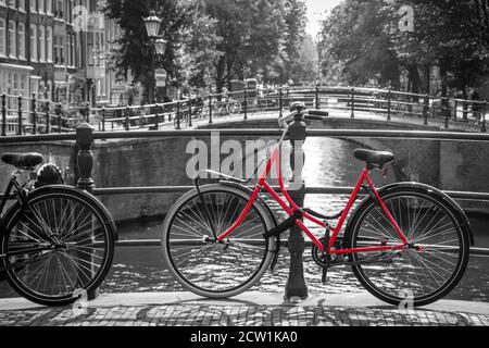 Una foto di una bici rossa sul ponte sul canale di Amsterdam. Lo sfondo è bianco e nero. Foto Stock