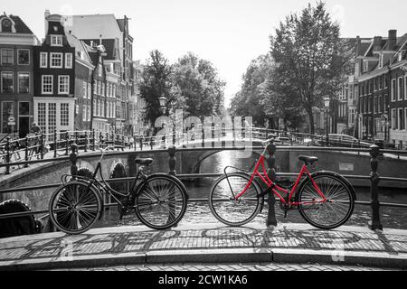 Una foto di una bici rossa sul ponte sul canale di Amsterdam. Lo sfondo è bianco e nero. Foto Stock