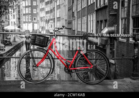 Una foto di una bici rossa sul ponte sul canale di Amsterdam. Lo sfondo è bianco e nero. Foto Stock