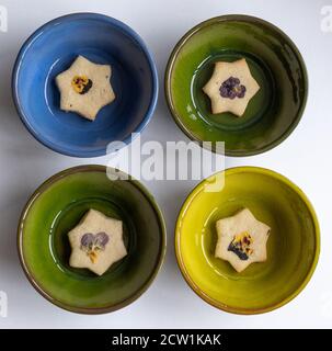 Biscotti a forma di stella decorati con fiori commestibili, pansies e petali di fiori di mais. Fotografato su sfondo di legno. Foto Stock