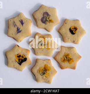 Biscotti a forma di stella decorati con fiori commestibili, pansies e petali di fiori di mais. Fotografato su sfondo di legno. Foto Stock