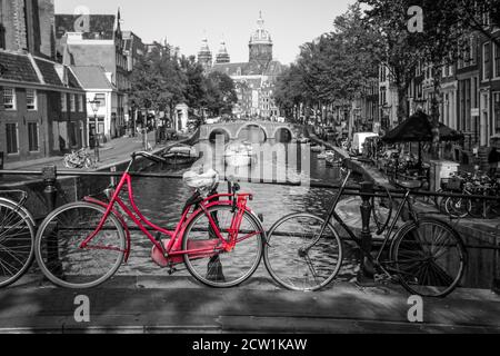 Una foto di una bici rossa sul ponte sul canale di Amsterdam. Lo sfondo è bianco e nero. Foto Stock