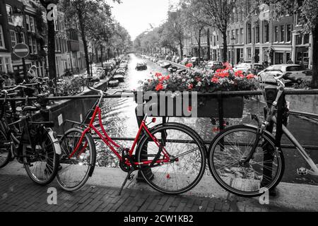 Una foto di una bici rossa sul ponte sul canale di Amsterdam. Lo sfondo è bianco e nero. Foto Stock