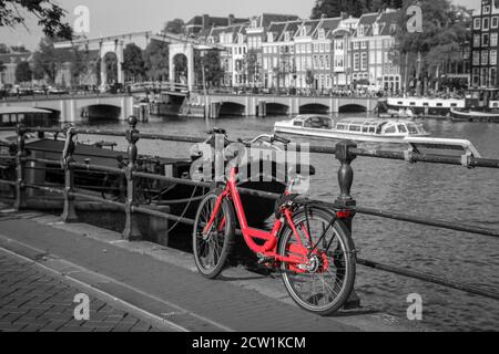 Una foto di una bici rossa sul ponte sul canale di Amsterdam. Lo sfondo è bianco e nero. Foto Stock