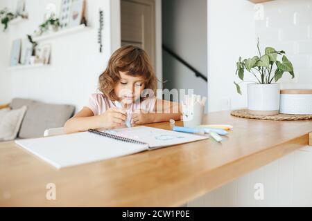 Carino ragazza felice, adorabile preschooler, 5 anni di pittura bambino al tavolo in un soggiorno bianco a casa. Concetto di scuola domestica Foto Stock