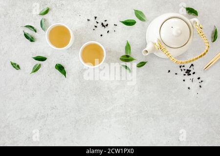 Tè alle erbe con due tazze da tè bianche e teiera, con foglie di tè verde. Disposizione piatta, vista dall'alto. Concetto di tè Foto Stock