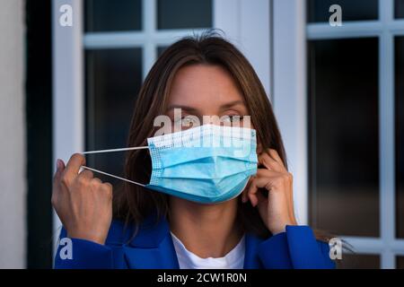 Bella donna mette su o toglie una maschera medica usa e getta. Protezione contro il coronavirus. Foto Stock
