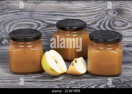 Marmellata di mele in vasi. Nelle vicinanze si trovano le fette di mela. Su tavole spazzolate, verniciate in bianco e nero. Foto Stock