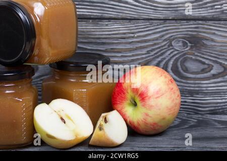 Marmellata di mele in vasi. Nelle vicinanze si trovano le fette di mela. Su tavole spazzolate, verniciate in bianco e nero. Foto Stock