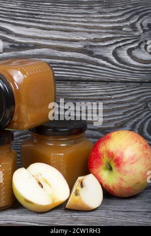 Marmellata di mele in vasi. Nelle vicinanze si trovano le fette di mela. Su tavole spazzolate, verniciate in bianco e nero. Foto Stock