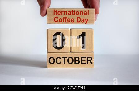 La mano maschile mette un blocco con l'iscrizione 'International coffee day' sui cubetti con la data del 01 ottobre. Splendido sfondo bianco, spazio per la copia. Foto Stock