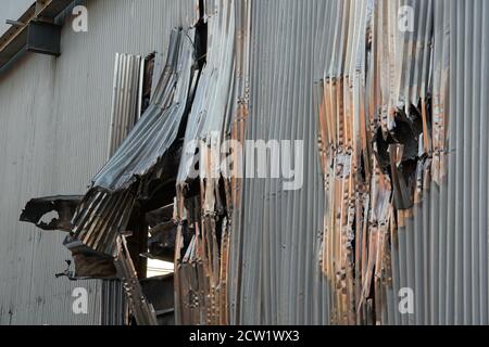 Vista ravvicinata sulla piastra corrugata in alluminio danneggiata dopo il fuoco come parte delle pareti della sala di assemblaggio industriale abbandonata della fabbrica. Foto Stock