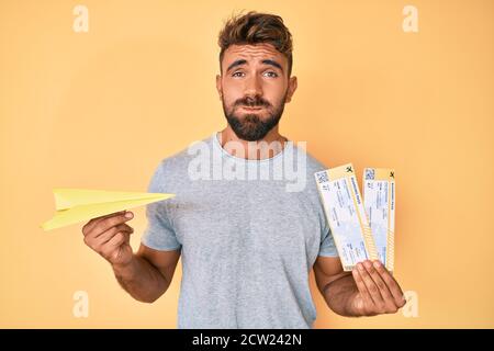 Giovane ispanico che tiene un aereo di carta e carta d'imbarco che soffica le guance con il viso divertente. Bocca gonfia con aria, prendendo l'aria. Foto Stock