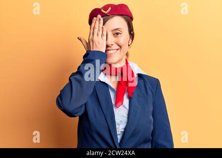 Giovane bella donna che indossa uniforme stewardess che copre un occhio con la mano, sorriso fiducioso sul viso e sorpresa emozione. Foto Stock