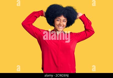 Giovane afroamericana che indossa abiti casual rilassante e stretching, braccia e mani dietro la testa e il collo sorridendo felice Foto Stock