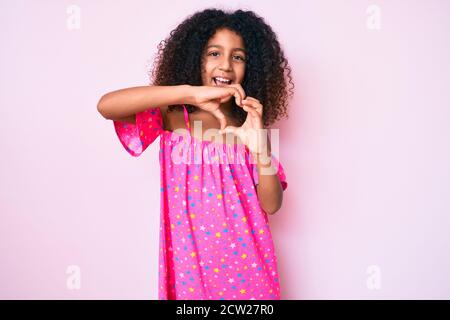 Bambino afroamericano con capelli ricci indossando abito casual sorridente in amore facendo il simbolo del cuore forma con le mani. Concetto romantico. Foto Stock