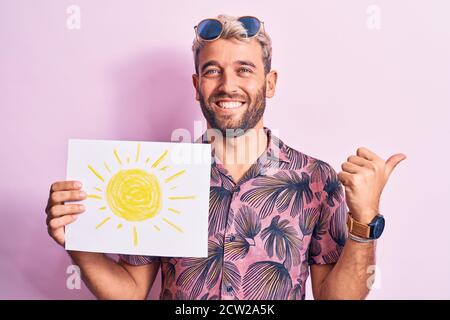 Bell'uomo turistico biondo in vacanza indossando occhiali da sole tenendo carta con il sole tirare il pollice verso l'alto sorridendo di lato felice con bocca aperta Foto Stock
