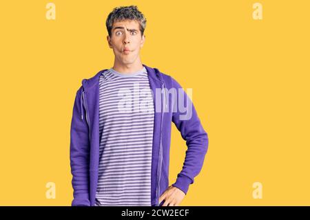 Giovane bell'uomo che indossa una felpa viola casual che fa viso di pesce con labbra, gesti pazzi e comici. Espressione divertente. Foto Stock