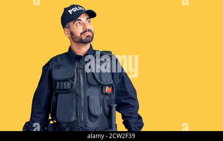 Giovane uomo ispanico che indossa uniforme della polizia sorridente guardando da parte e fissando via pensare. Foto Stock