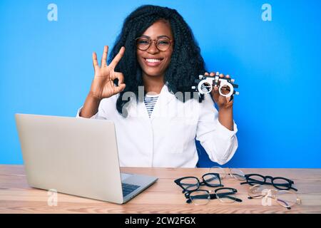 Bella donna africana che tiene occhiali di optometria facendo ok segno con le dita, sorridente amichevole gesturing eccellente simbolo Foto Stock