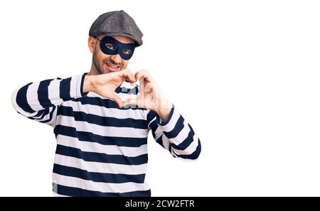 Giovane bell'uomo che indossa una maschera di scasso sorridente nell'amore facendo il simbolo del cuore forma con le mani. Concetto romantico. Foto Stock