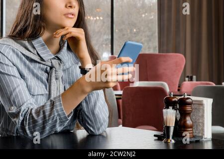 Triste bella giovane donna con smartphone in attesa di fidanzato ristorante Foto Stock