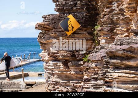 Pericolo caduta rocce segno come surfer si dirige verso l'oceano, Sydney, NSW, Australia Foto Stock