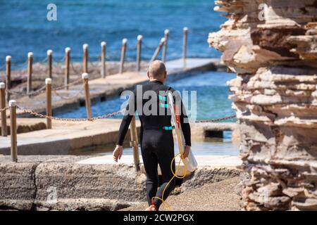 Surfista australiano di sesso maschile che trasporta la tavola da surf all'oceano Foto Stock