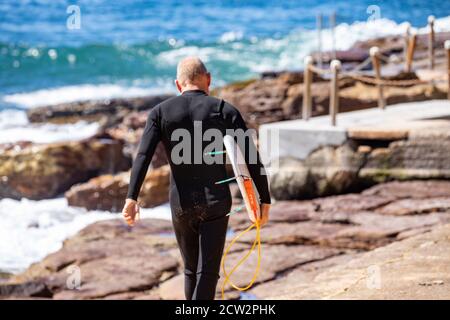 L'uomo australiano di mezza età che indossa muta cammina verso il surf Con la sua tavola da surf, Sydney, NSW, Australia Foto Stock