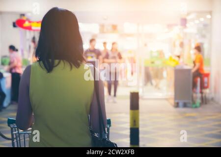 Lato posteriore di Donna shopping in Supermarket Aisle e Shelves prodotto in blurry per sfondo. Foto Stock