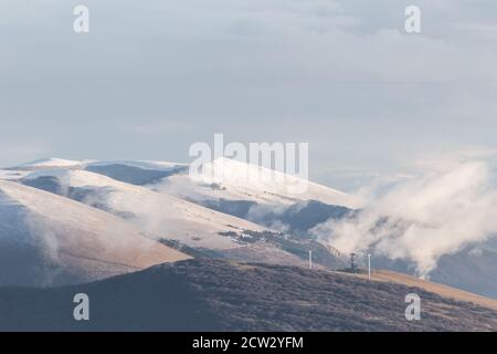 Montagna (Umbria, Italia) in inverno, coperta di neve, con nuvole basse e turbine eoliche Foto Stock