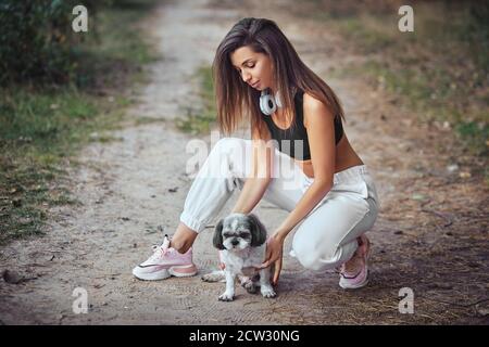 Una giovane donna con il suo carino Shih Tzu è seduta su un sentiero nei boschi. Foto Stock