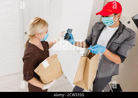 Consegna uomo che tiene sacchetto di carta con cibo su sfondo bianco, uomo di consegna di cibo in maschera protettiva Foto Stock