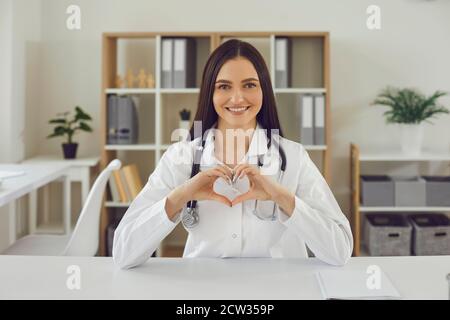 La giovane dottoressa mostra in webcam un segno d'amore per il paziente che fa un cuore con le mani. Foto Stock