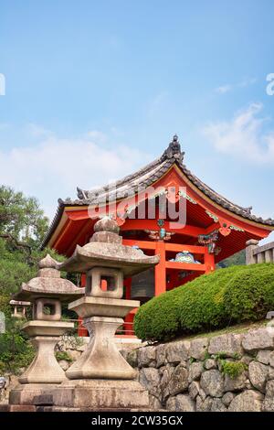 La vista del luminoso campanile vermiglio (shoro) del tempio Kiyomizu-dera con le due lanterne in pietra toro in primo piano. Kyoto. Giappone Foto Stock