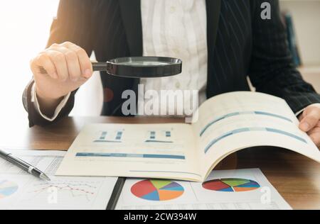 Le donne di affari che usano la lente di ingrandimento per rivedere il rapporto di sintesi finanziario. Concetto di audit interno, Auditing tax, analisi del rendimento degli investimenti. Foto Stock