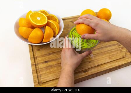 Vista delle mani che strizzano le arance con una centrifuga sulla parte superiore di un tagliere di legno Foto Stock
