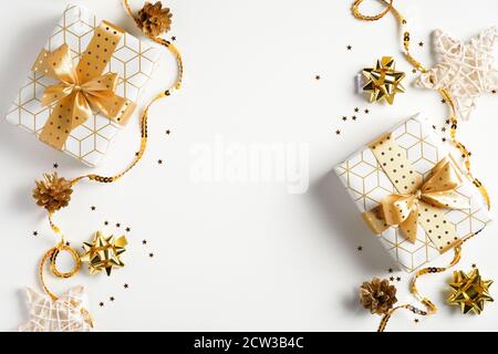 Piatto posa di Natale composizione. Confezioni regalo vista dall'alto, decorazioni dorate, nastri, confetti su sfondo bianco. Natale, vacanze invernali, Capodanno c Foto Stock