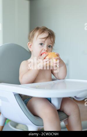 Bambino che mangia una mela seduto su sedia alta Foto Stock