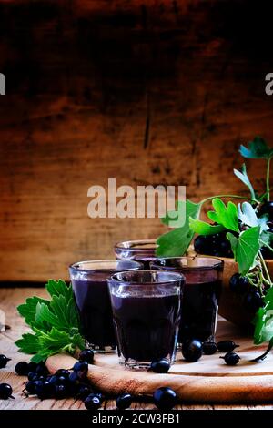 Liquore fatto in casa a base di ribes nero e frutti di bosco freschi, fondo in legno vintage, fuoco selettivo Foto Stock