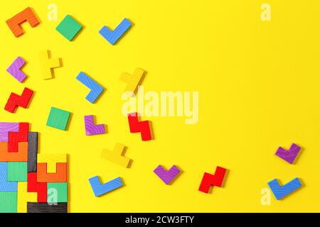 Diverse forme colorate blocchi di puzzle in legno su sfondo giallo. Forme geometriche in colori diversi, vista dall'alto Foto Stock