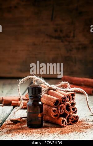 Olio essenziale di cannella in una piccola bottiglia, cannella macinata e bastoncini di cannella su vecchio sfondo di legno, fuoco selettivo Foto Stock