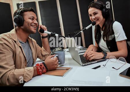 Portait di due felici padroni di casa della radio, giovane uomo e donna che parlano tra loro mentre moderano uno spettacolo dal vivo in studio Foto Stock