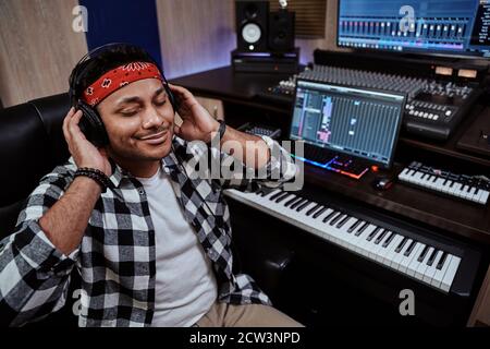 Giovane uomo, artista maschile in cuffia seduto con gli occhi chiusi mentre si ascolta la musica in studio di registrazione Foto Stock