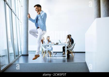 Giovane uomo d'affari con smartphone saltando in un ufficio moderno e. esprimere entusiasmo Foto Stock