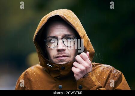 Pioggia intensa durante il giorno d'autunno. Ritratto di giovane uomo in giacca impermeabile. Foto Stock