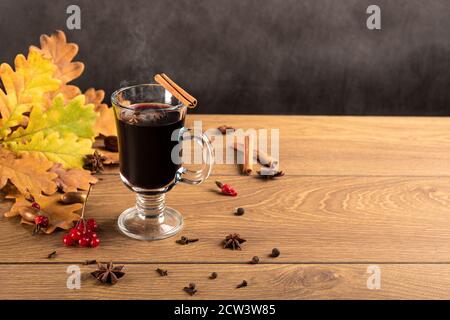 VIN brulé in tazzine di vetro con cannella e anice su un tavolo di legno. Sfondo di foglie di quercia caduto. Copyspace autunno Foto Stock