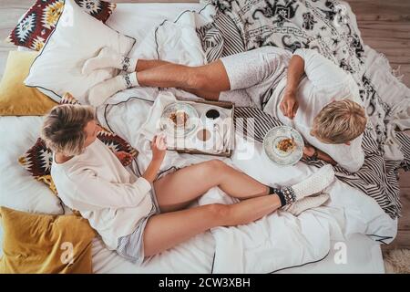 Vista dall'alto della coppia in pigiama rilassante sdraiata in un comodo letto in camera da letto e con un caffè mattutino con dessert a torta di mele. Si spensierano peacefu Foto Stock