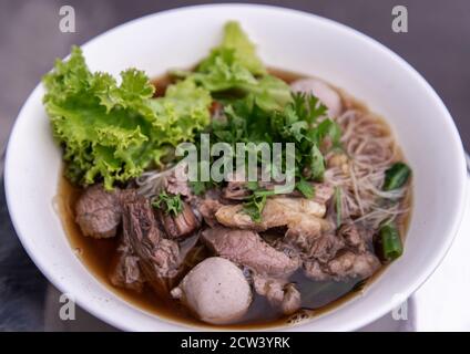 Primo piano di zuppa di manzo tailandese chiaro spaghetti di riso bianco vermicelli con manzo brasato, polpette e verdure. Delizioso fast food di strada in Thailandia. No Foto Stock